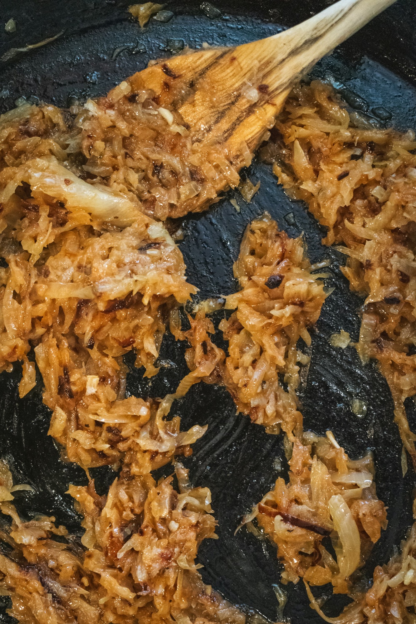 Deep golden caramelized onions in a cast iron pan, being stirred with a wooden spoon