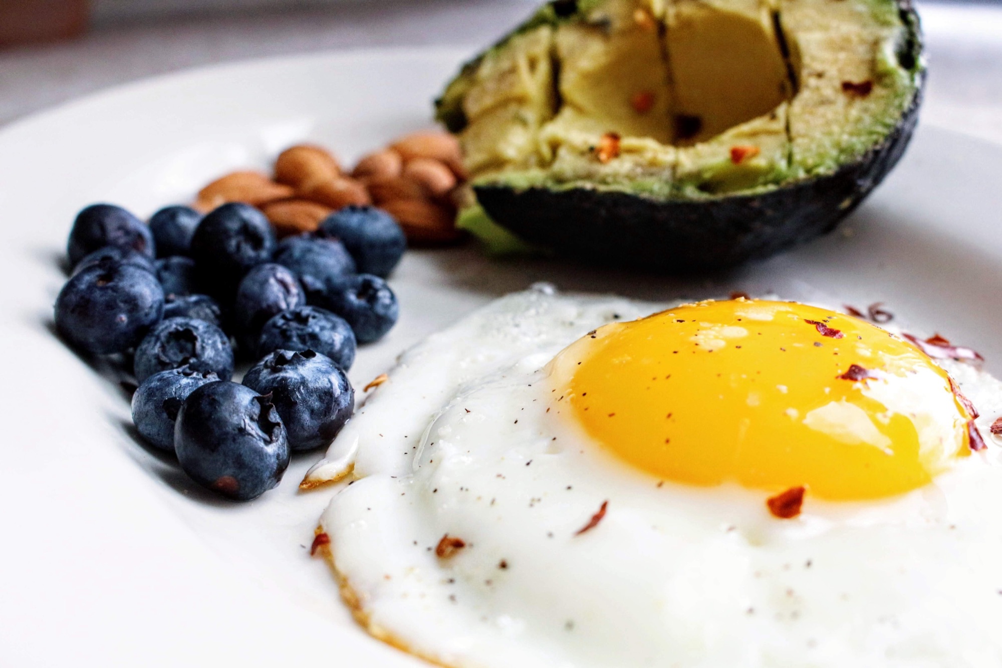 A plate with a fried egg, avocado, almonds, and blueberries — protein, fat, and carbohydrate sources together