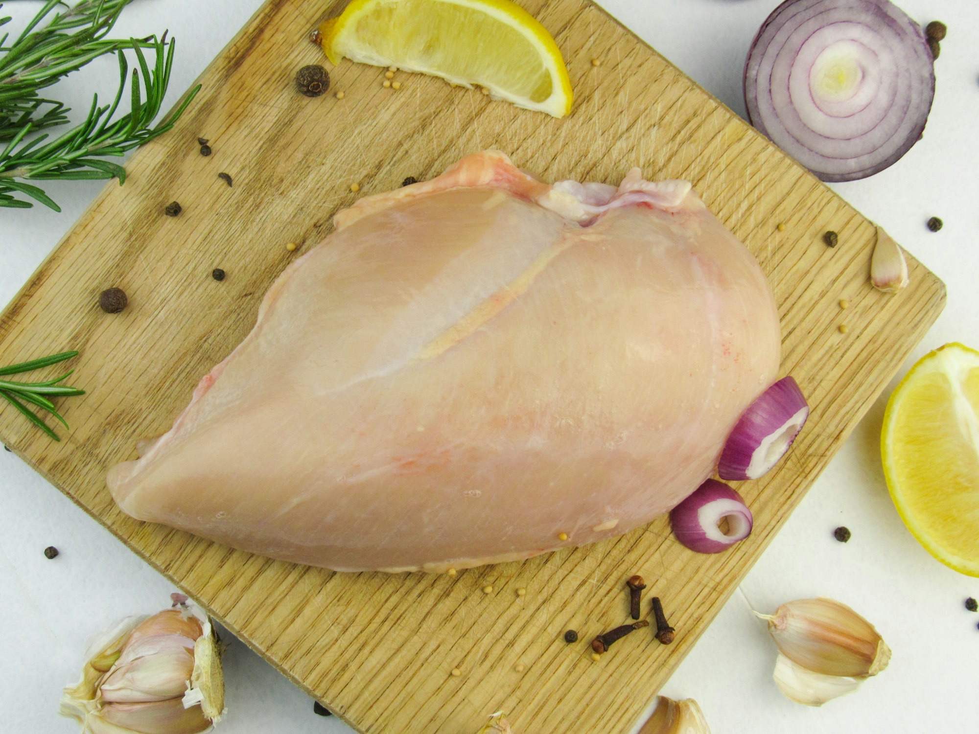 Raw chicken breast with lemon, garlic, onion, and rosemary, ready to marinate