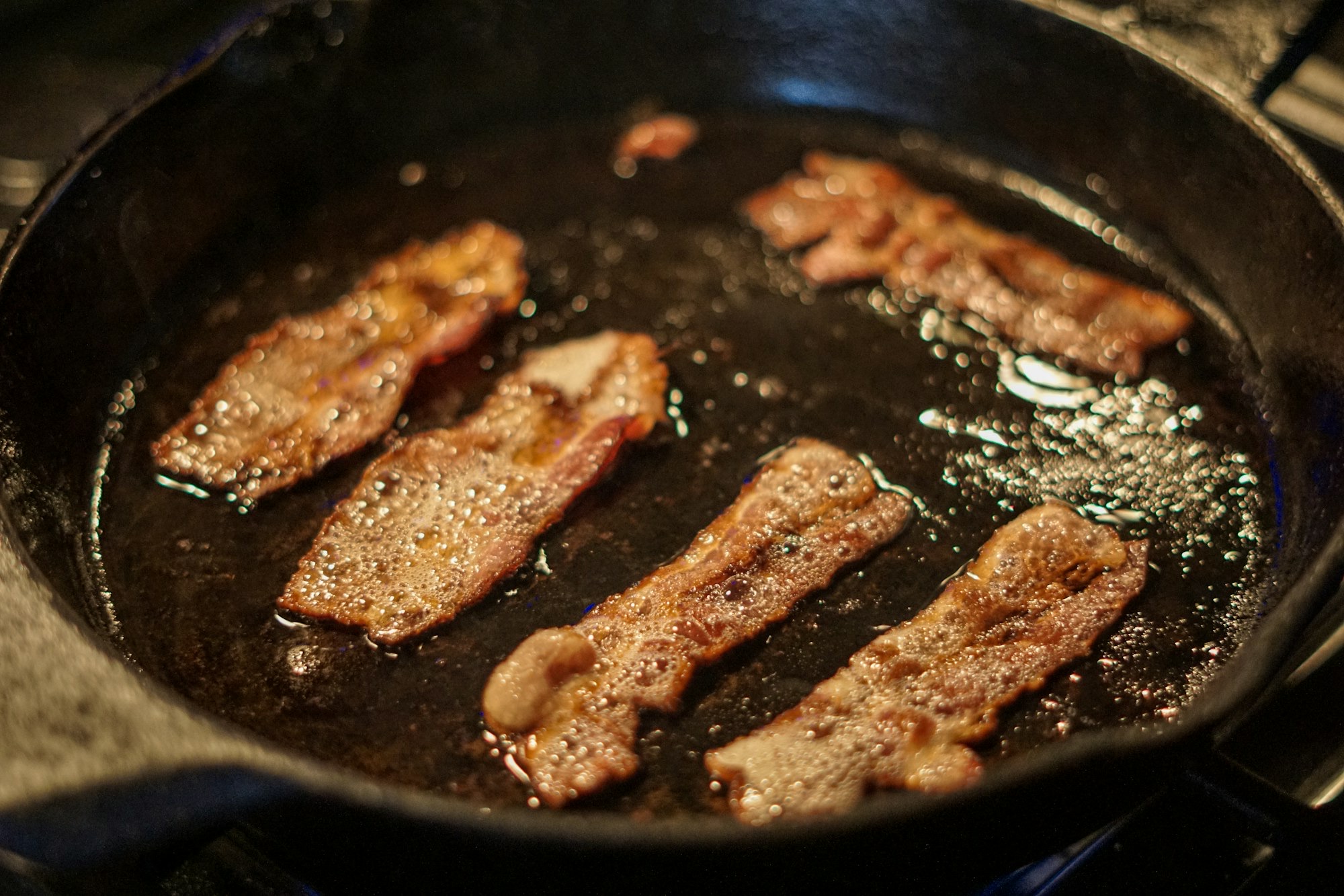 Bacon strips searing in a cast iron pan