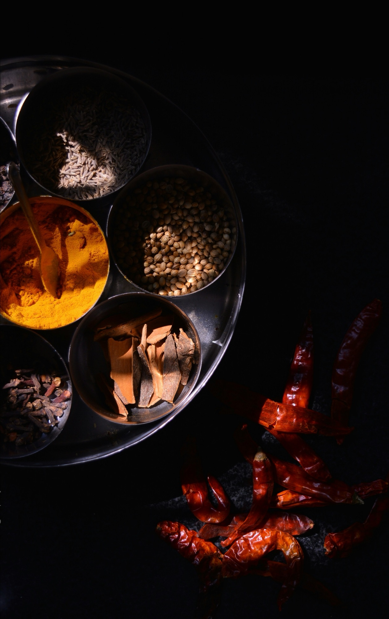 A tray of whole Indian spices — cumin, coriander, cinnamon, turmeric, and dried chilies